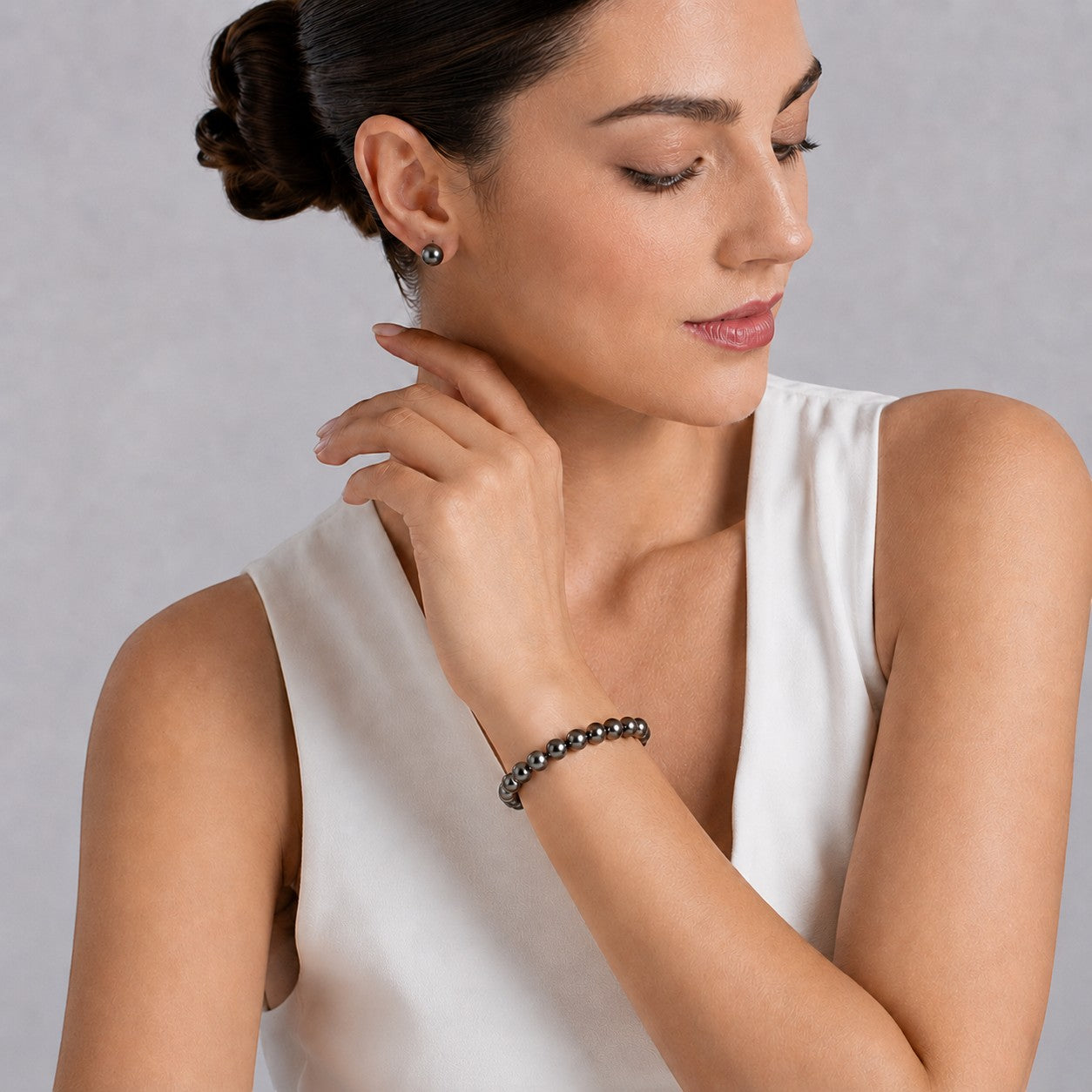 Prestige Pearl 8-9mm round black Tahitian pearl bracelet worn by a woman in a white top with matching pearl earrings